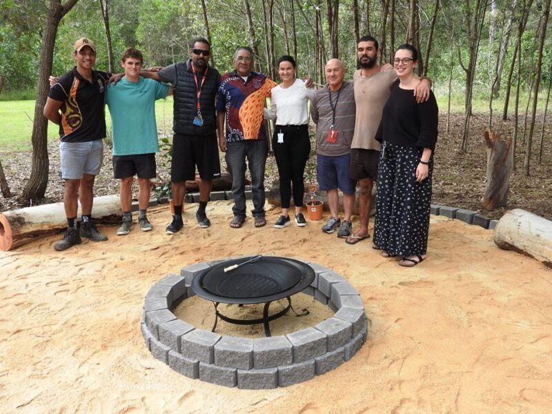 Group of Anglicare workers and stakeholders posed around yarning circle at Carbrook