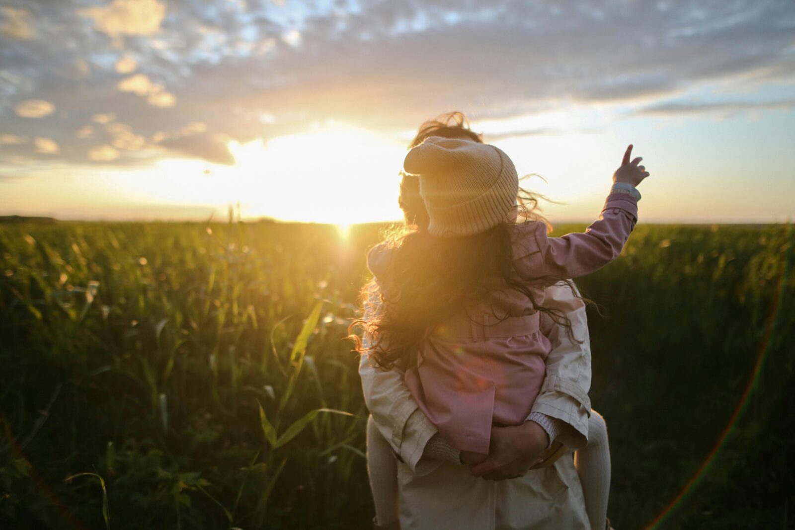 Children are happy when they feel safe. Mother holding young daughter in a field at sunset.