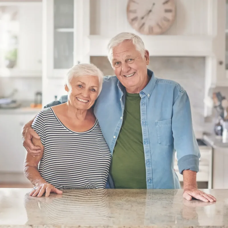 Elderly kinship carers standing in their kitchen.