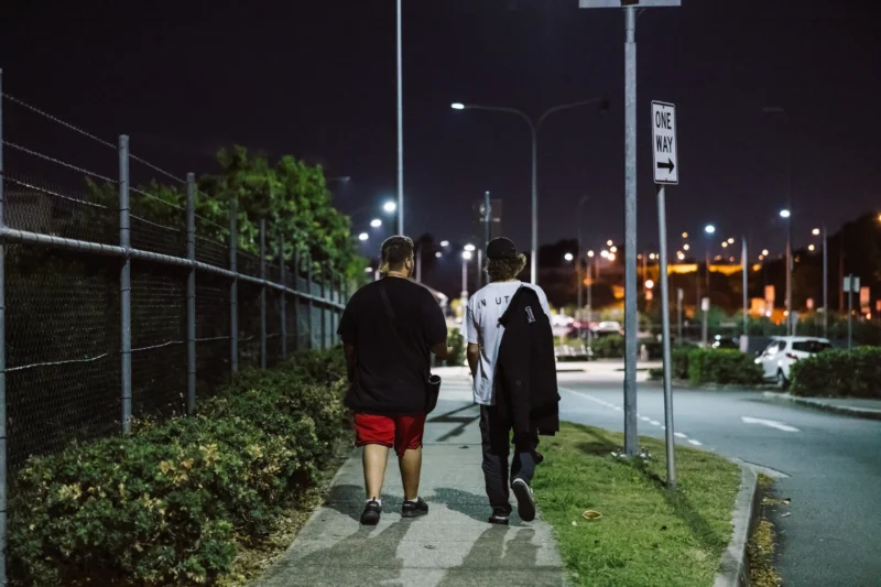 Two male youth homelessness service clients walking down a city street at night, seeking safety and support.