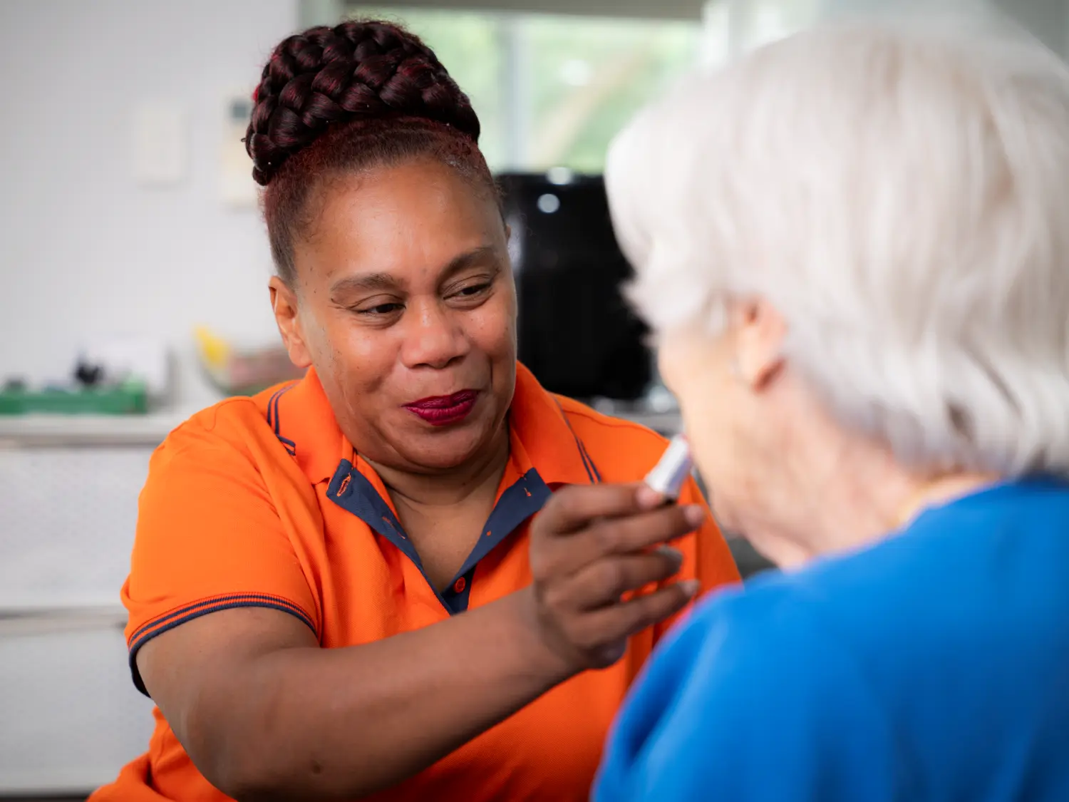 Anglicare staff member helping client put lipstick on.