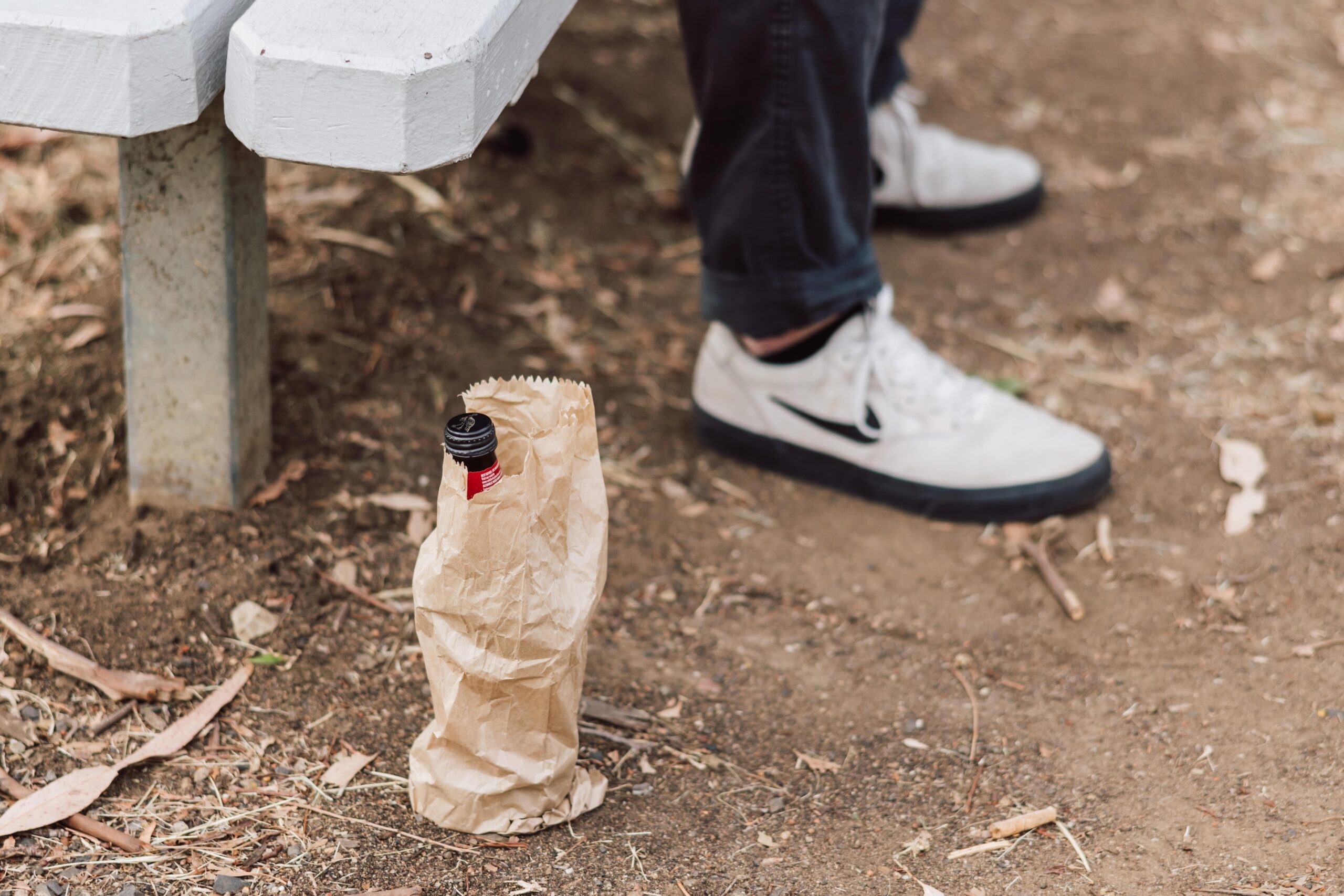 Young person sitting on bench with a bottle of alcohol