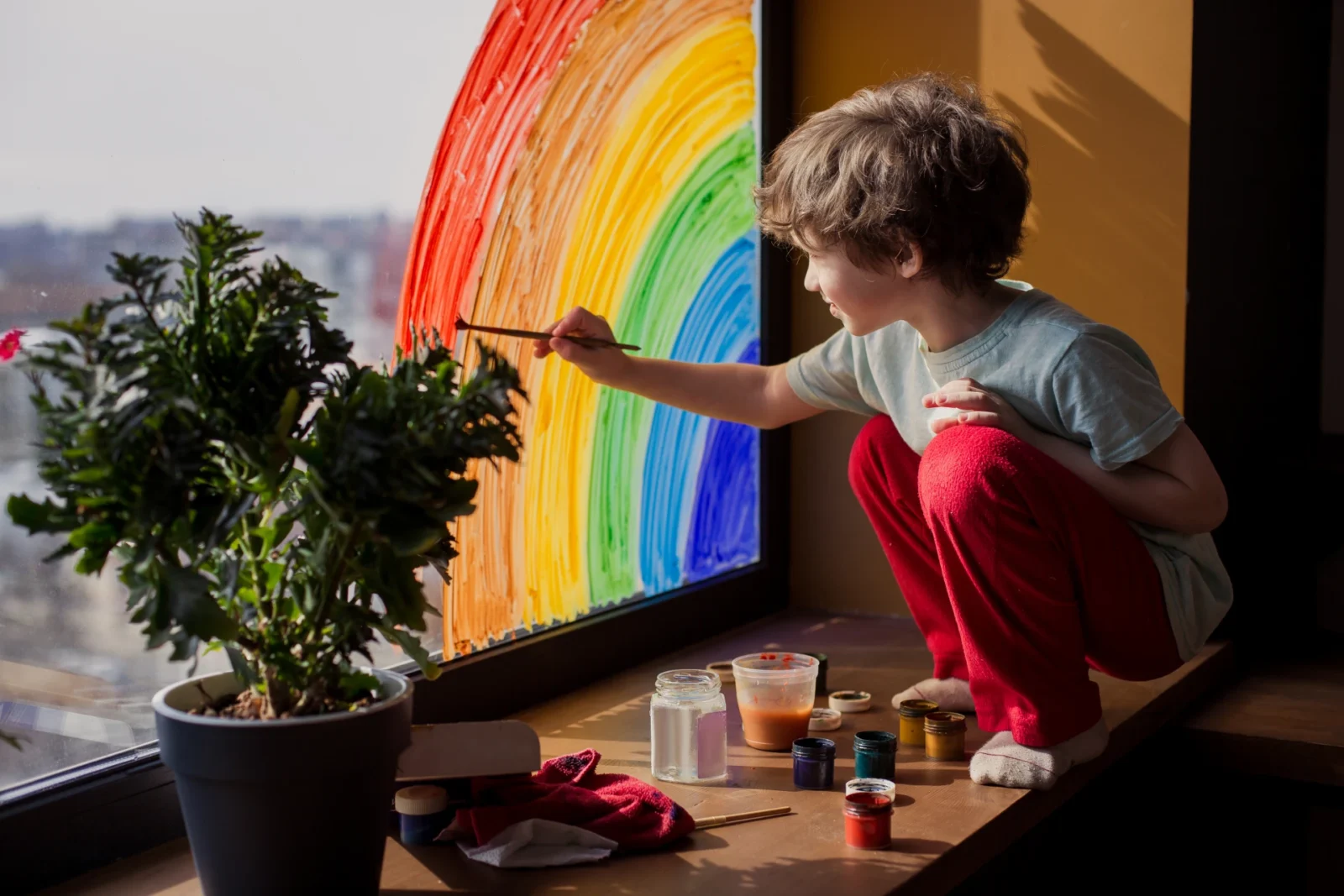 Little boy painting a rainbow on a window.