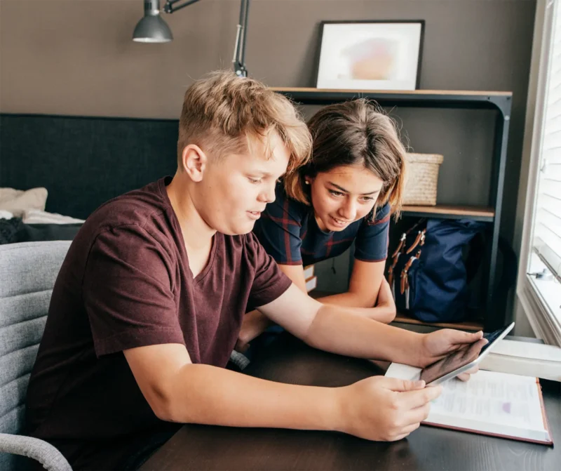 Young teenage boy and girl sitting at a desk looking at an iPad.
