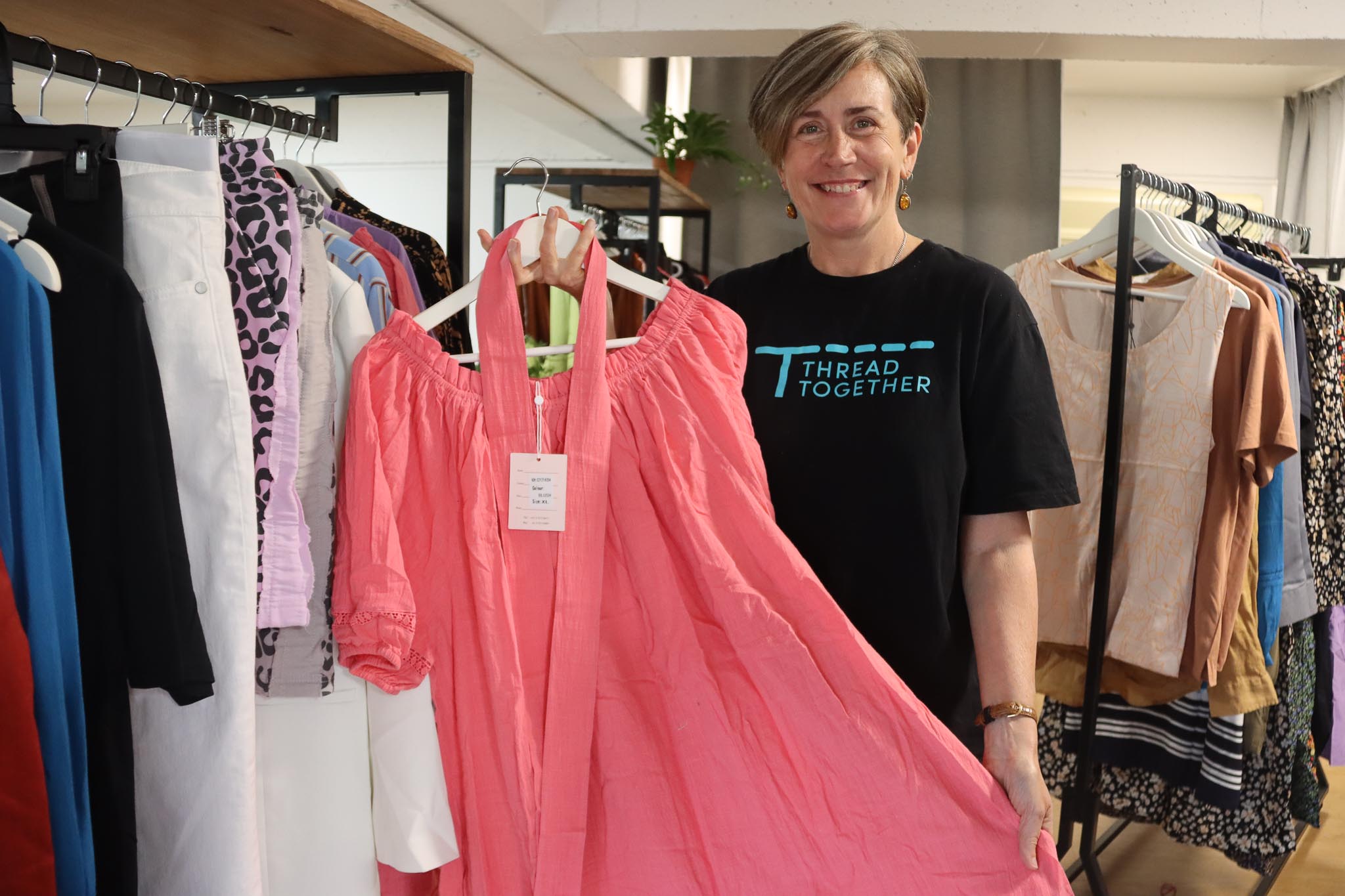 Kate Littmann-Kelly, Thread Together Coordinator, holding up one of the pink dresses from the St Andrew's Clothing Hub.