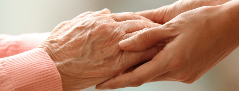Carer compassionately holding loved ones hand