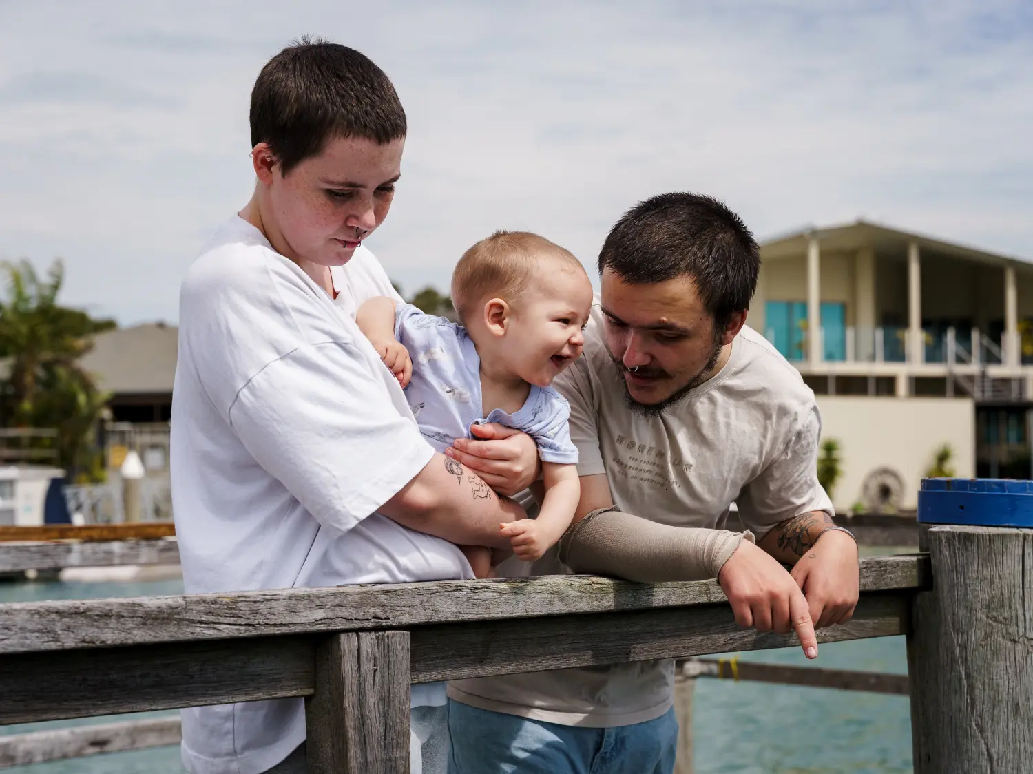 Noah, Venus, and baby Eli standing together on a wooden deck by the water, representing a young family receiving support through Anglicare’s Christmas Appeal to help homeless youth.