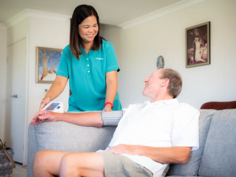 Respite carer checking a man’s blood pressure on a couch during in home respite care.