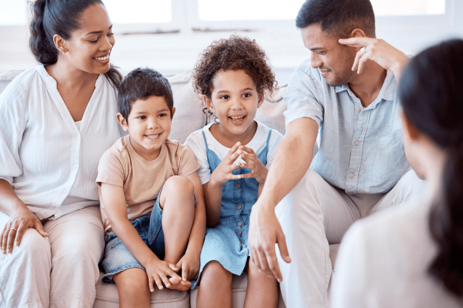 A young family with two children sitting down to do family counselling with a female counsellor