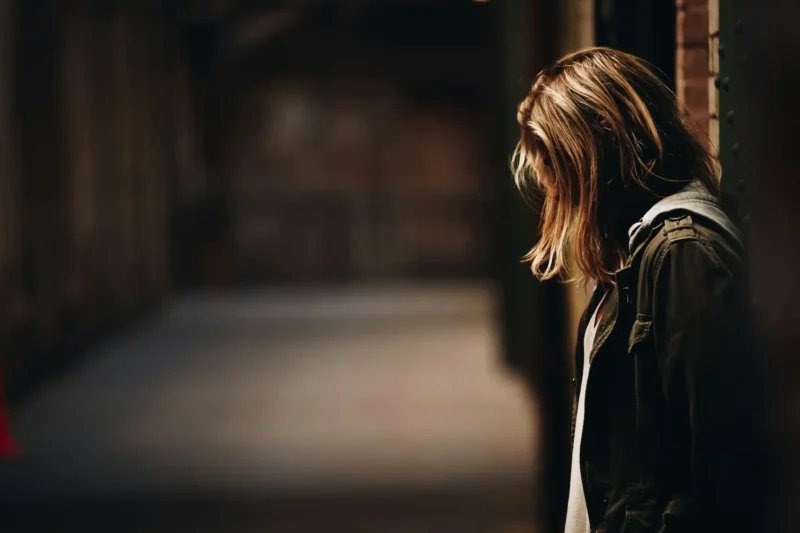 Homeless youth client standing alone in a dimly lit hallway at night, illustrating vulnerability and the need for support from youth homelessness services.
