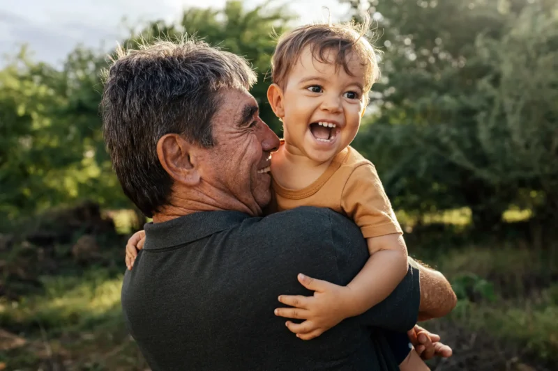 Guardian holding a smiling young child in a garden.