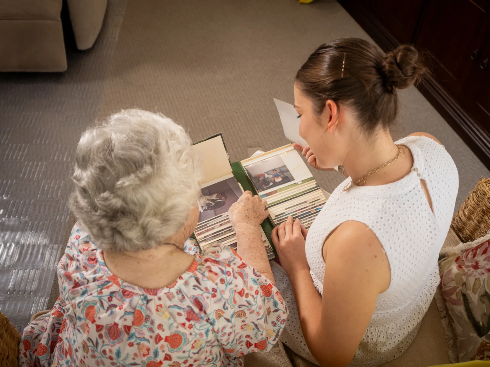 Young woman volunteering time with elderly client who is showing her a photo album.