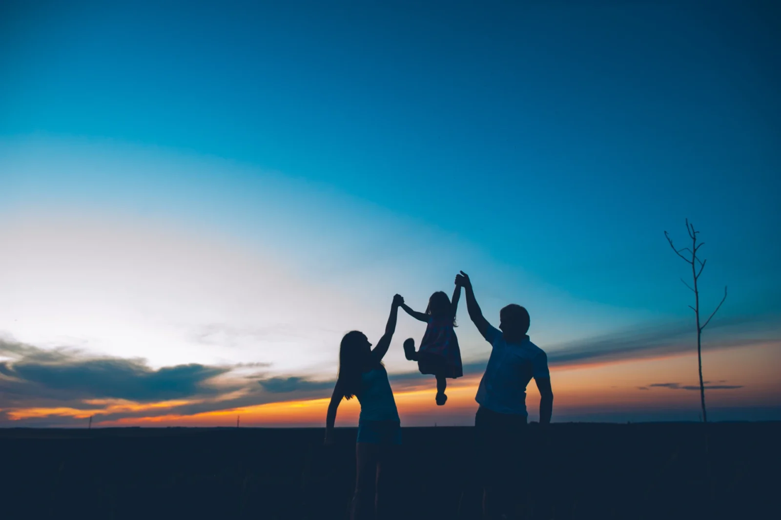 silhouette of two parents swinging their child as the sun sets