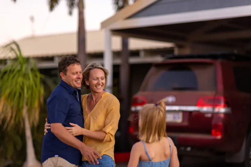 Carer couple spending time together outside their home while a child approaches, illustrating how respite foster care supports important family time and strengthens relationships.