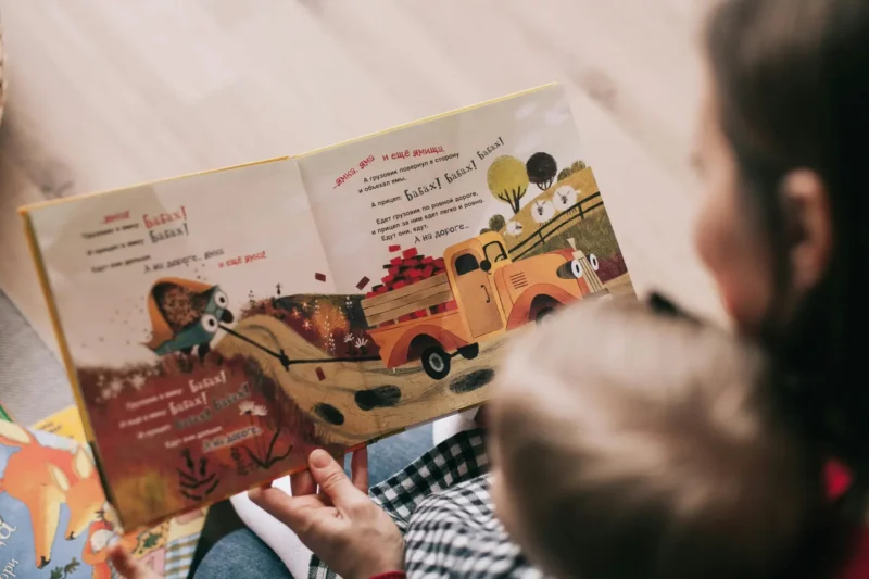 Carer reading a colorful picture book with a child, showing the nurturing and educational benefits of respite foster care.