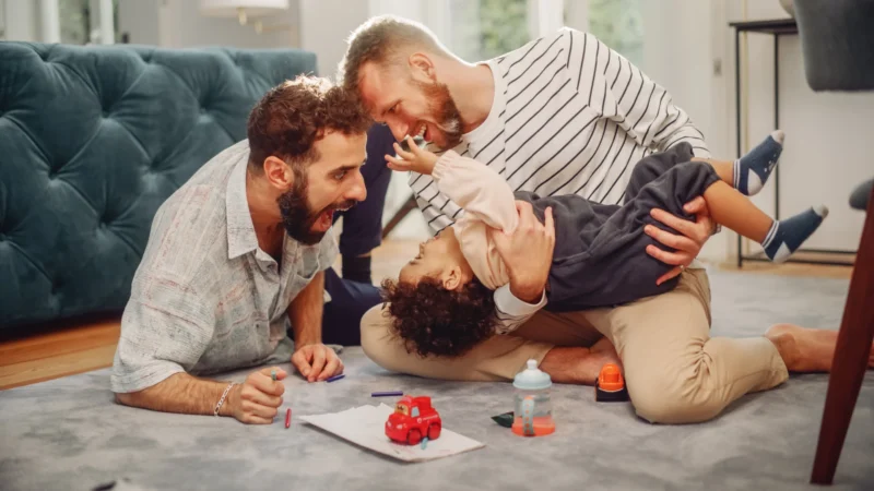 Two male foster and kinship carers playing with foster child
