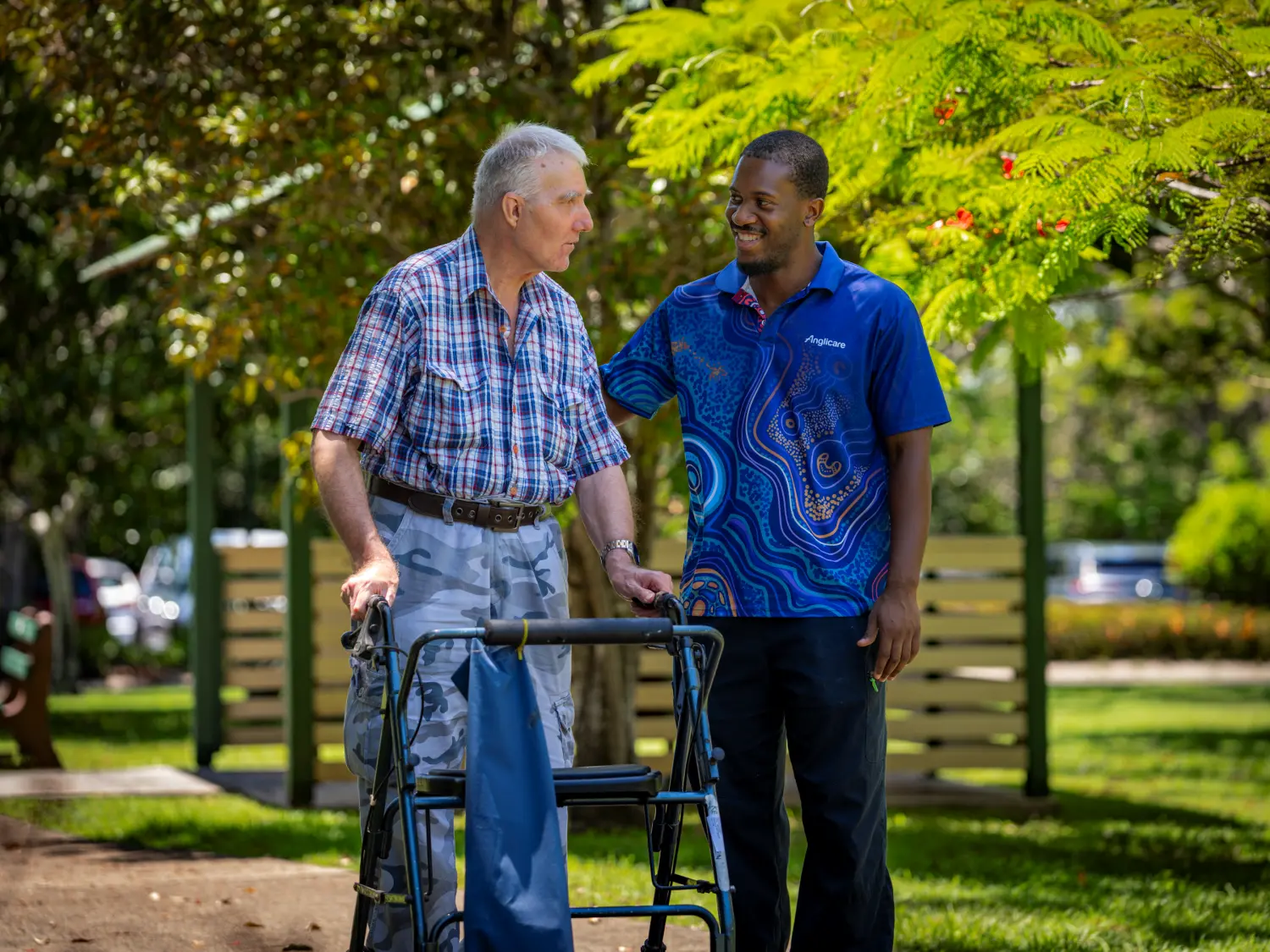 Anglicare Southern Queensland aged care worker supporting elderly client to walk with her wheelie walker.