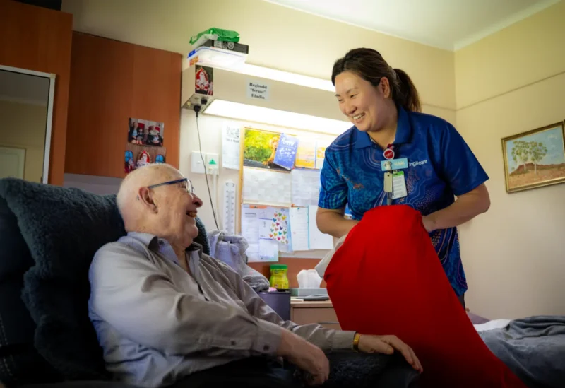 Anglicare Southern Queensland female nurse holding elderly patient's hand.
