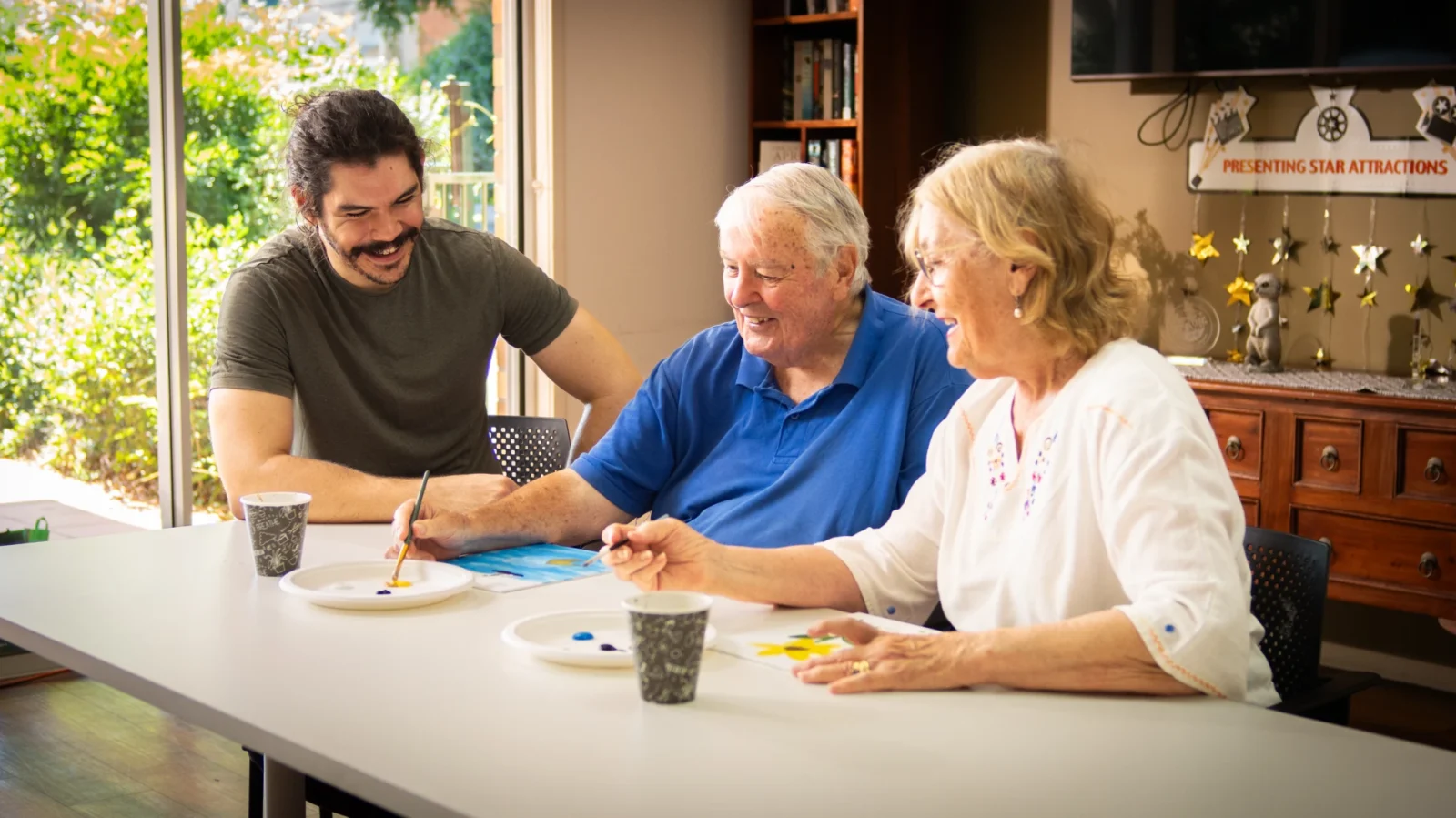 Young man volunteering his time to help elderly couple with a painting activity.