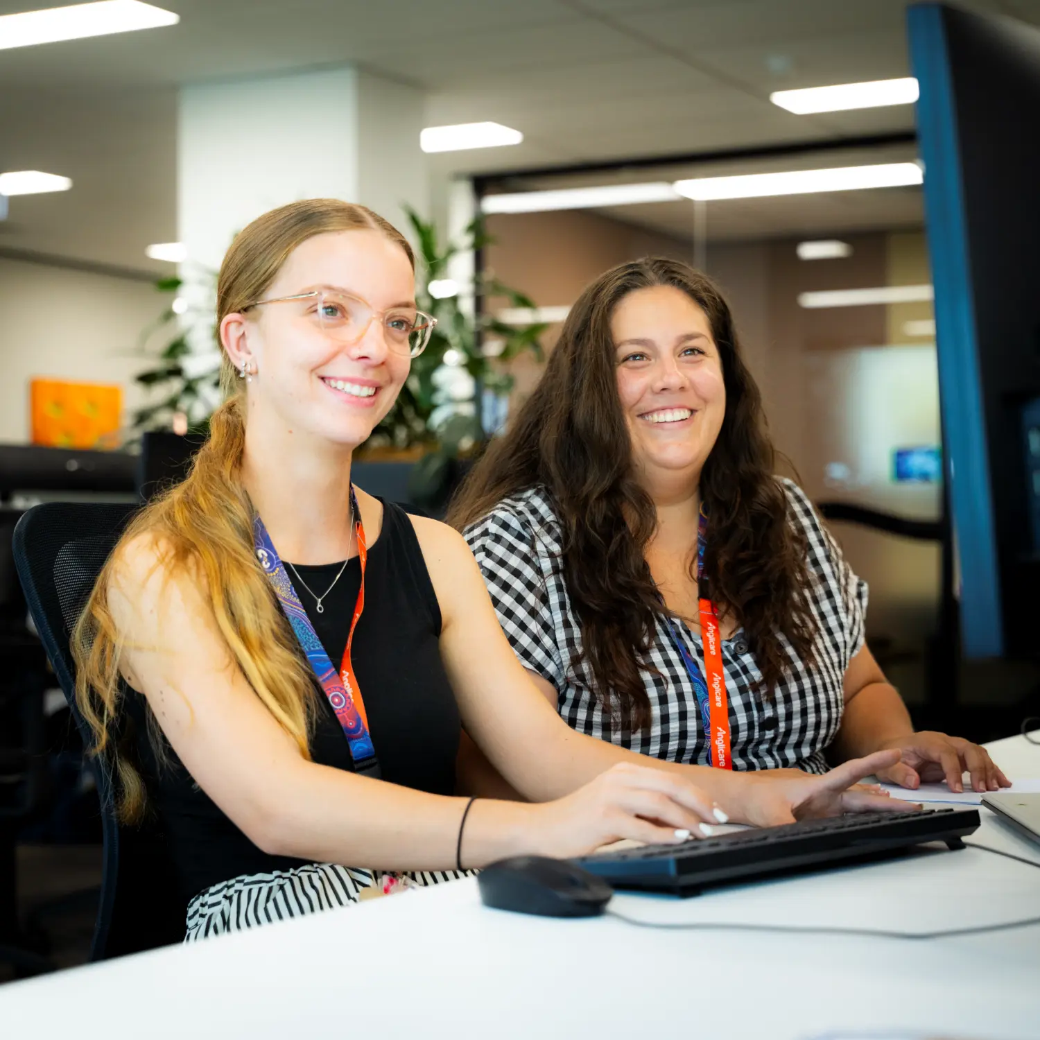 Two Anglicare workers sitting at desk on computer