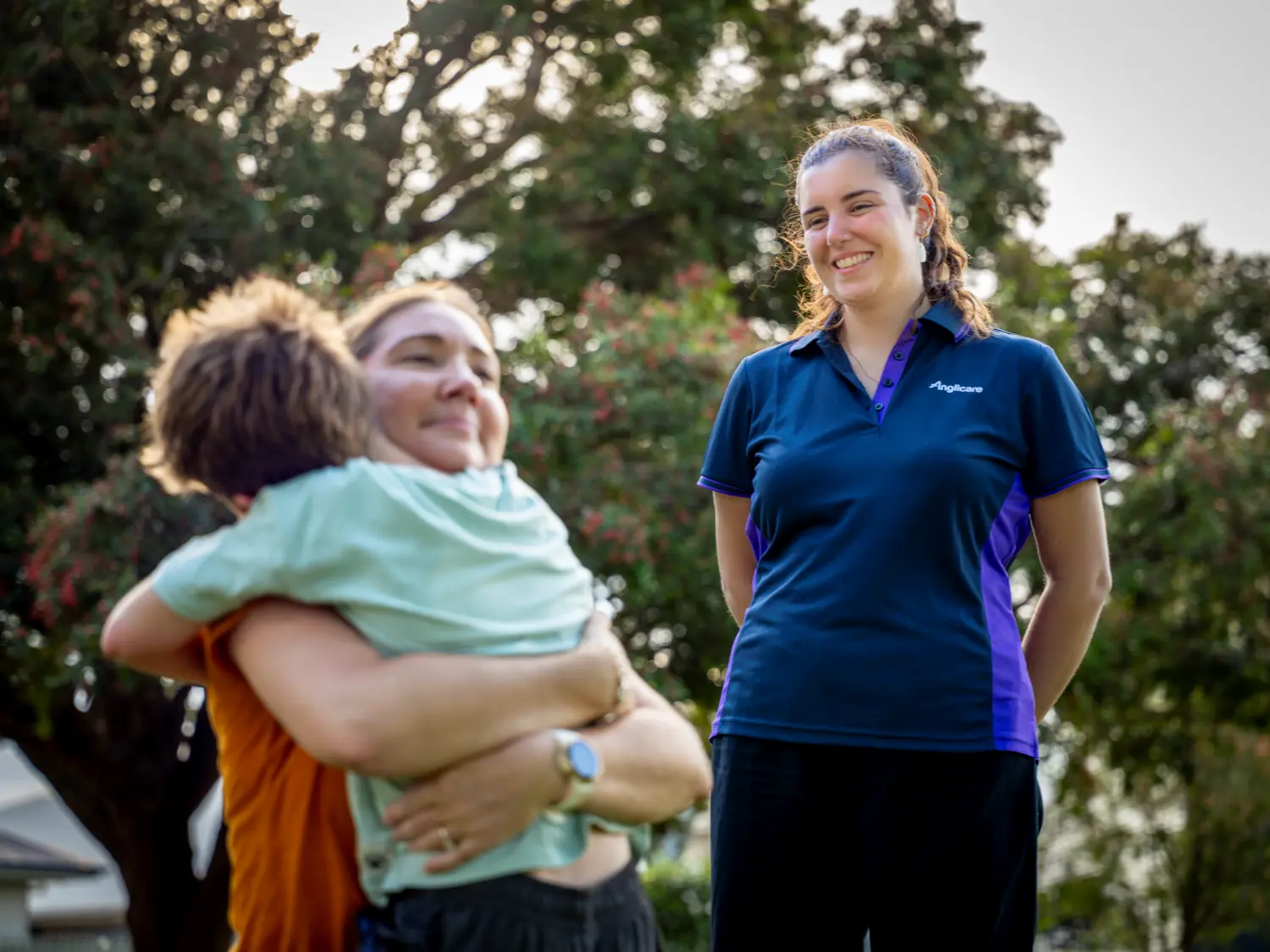 Mother hugging child with Anglicare family worker watching