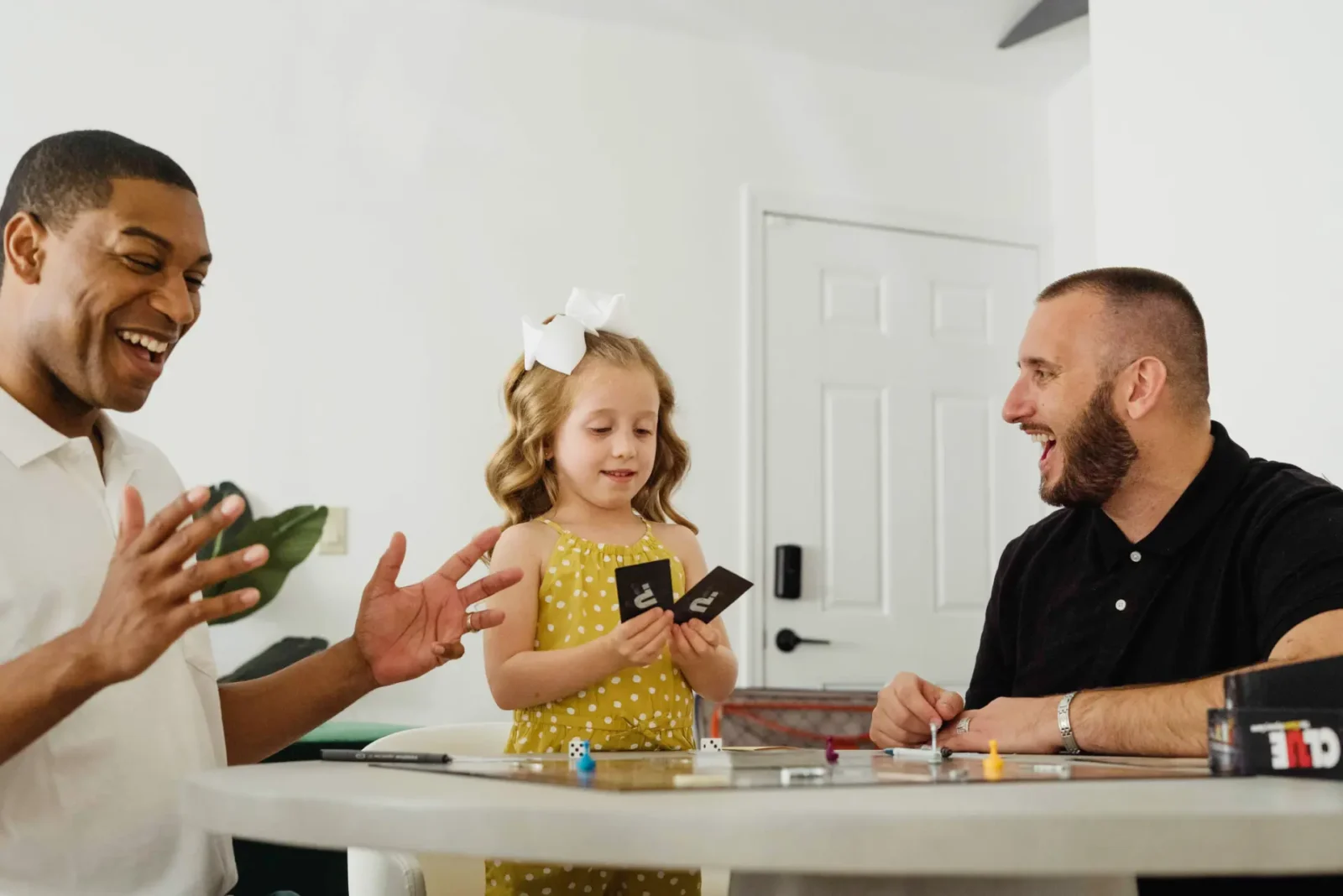 Two male foster carers playing card game with young girl.