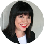 A woman with straight black hair and a fringe, wearing a black blazer and white top, smiles at the camera against a light-coloured background.