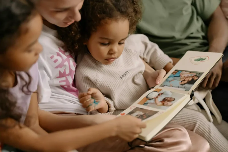 Kinship carer and two children sitting together indoors, looking at a photo album and smiling.