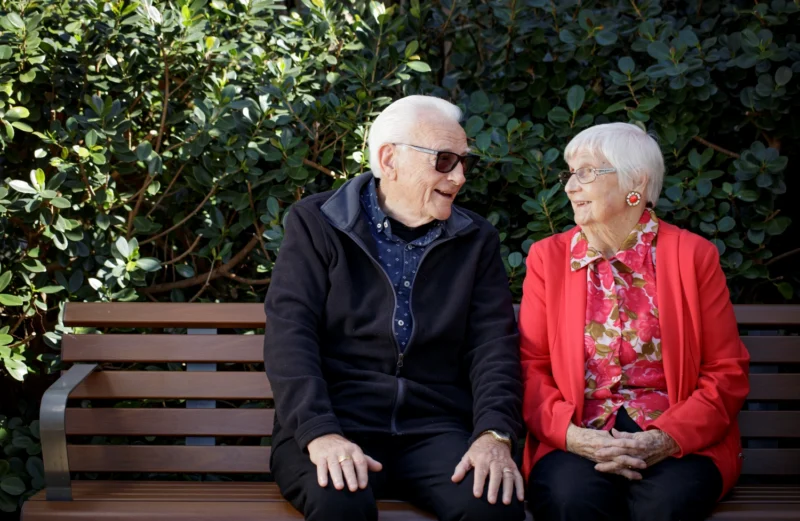Two older people seated together on a bench, illustrating dementia care that supports family connection and helps reduce carer stress.