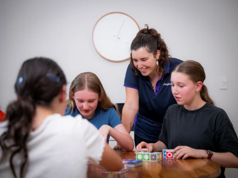 Youth worker smiles whilst interacting with three girls in youth residential care, engaging with colourful blocks.