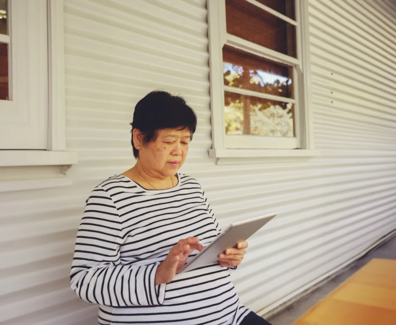 Older woman using a tablet independently while receiving flexible respite care services at home.