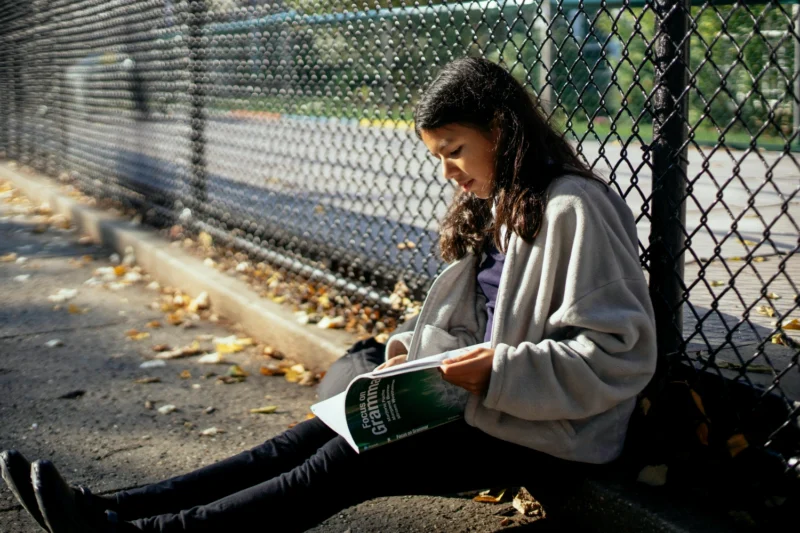 Picture of young person in youth residential care sitting against fence and reading a text book