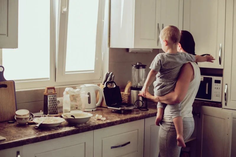 Mother in kitchen holding her son while making breakfast.