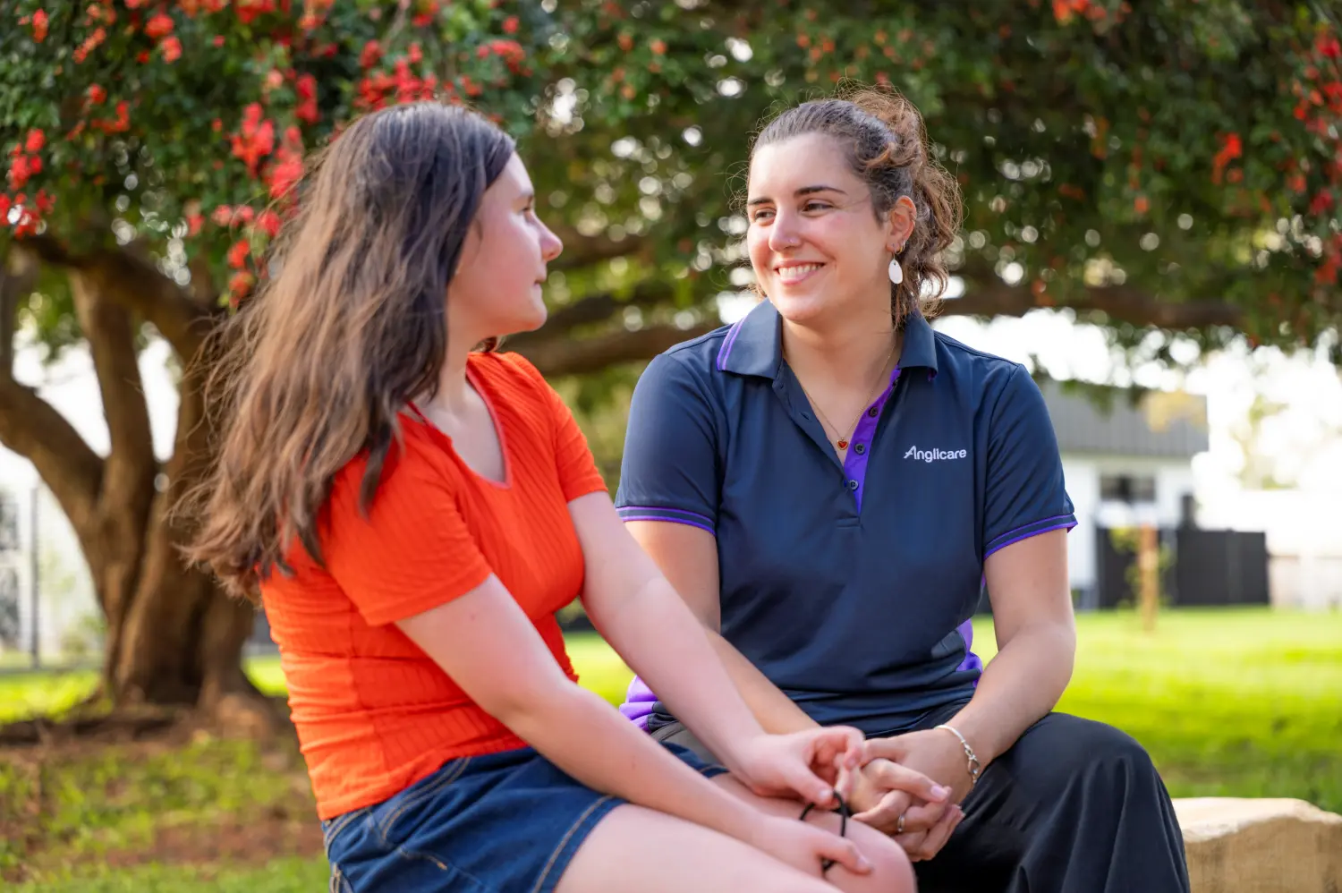 female youth homelessness client sitting on a bench and talking to an Anglicare worker.