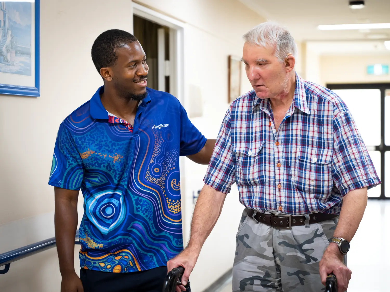 Anglicare worker helping elderly male resident walk through aged care home