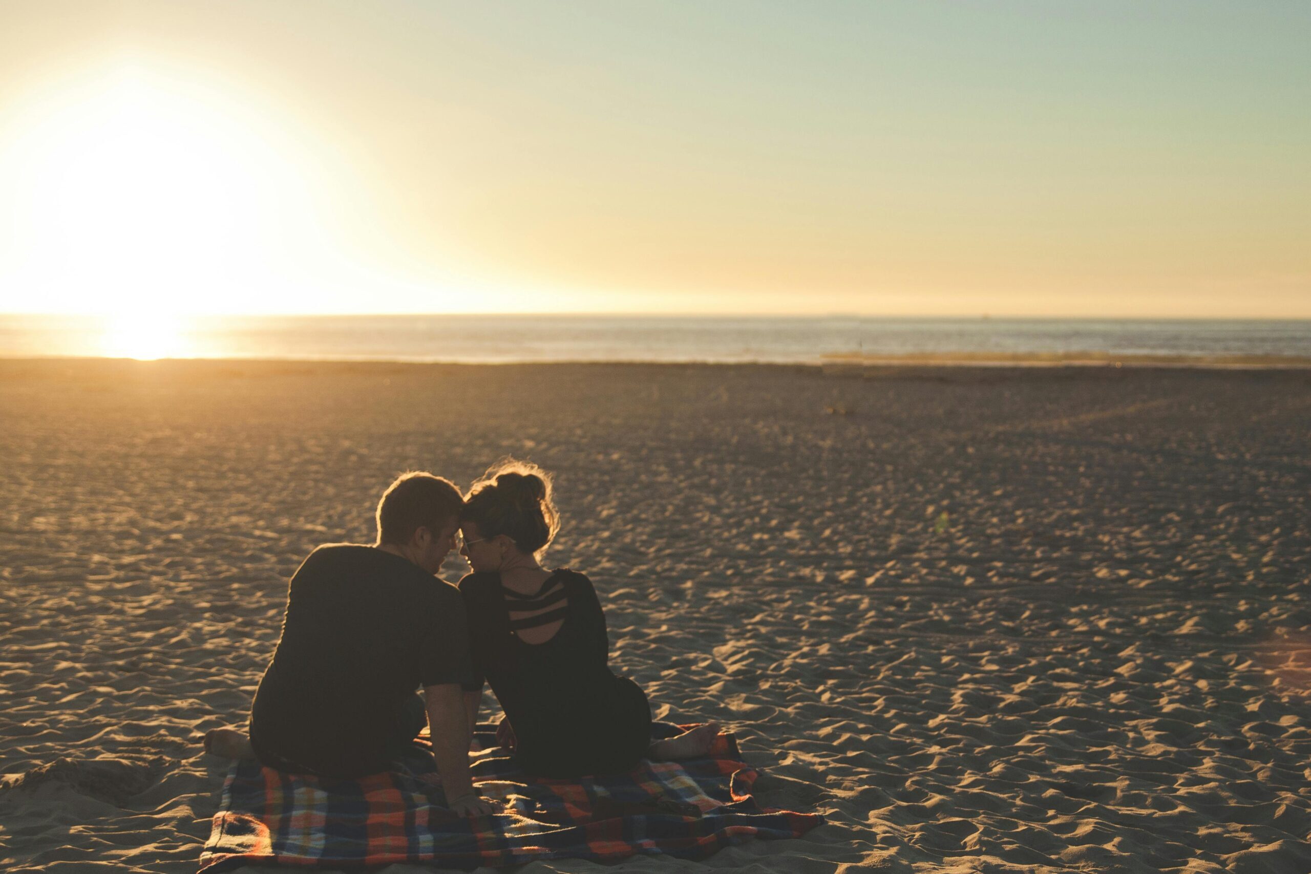 Stages of a relationship. Couple sitting on the beach looking into each others eyes.