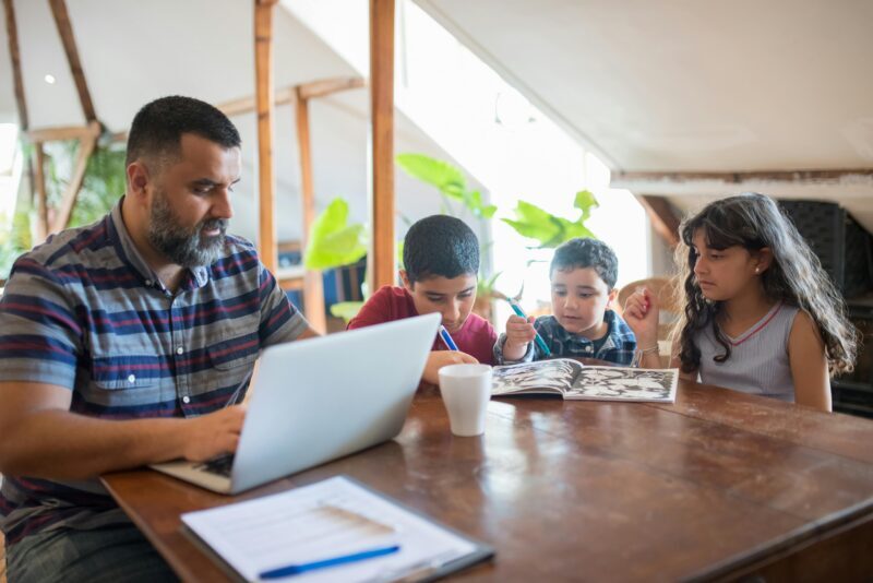 Parent exhibiting work-life balance at table with children beside him.