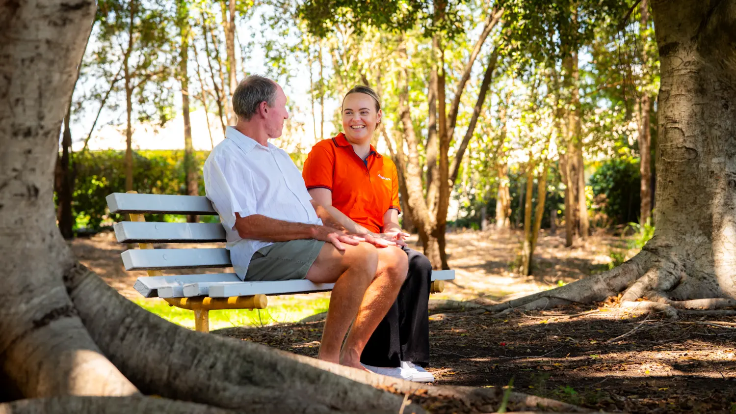 Anglicare worker sitting with male client on park bench outdoors