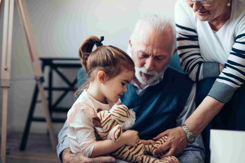 young girl sitting with elderly man and woman, holding her toy